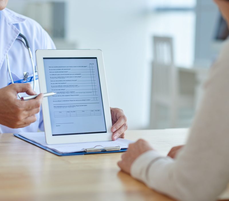 Close-up shot of physician pointing at screen of digital tablet, female patient listening to him with concentration